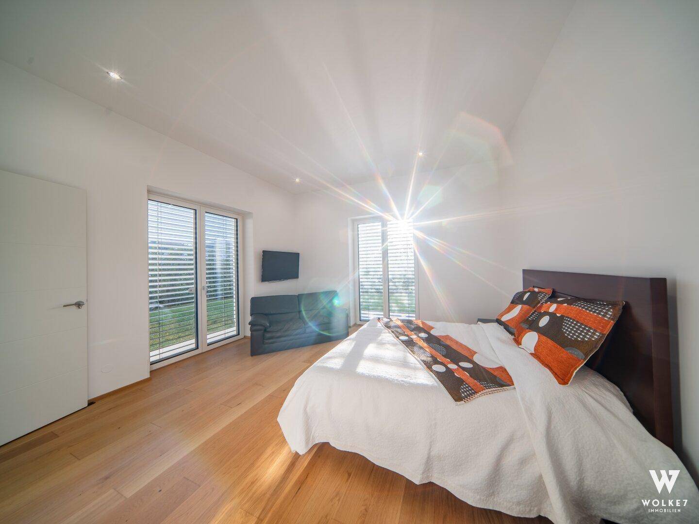 Sonniges Schlafzimmer mit Holzboden, großen Fenstern und modernen Jalousien.