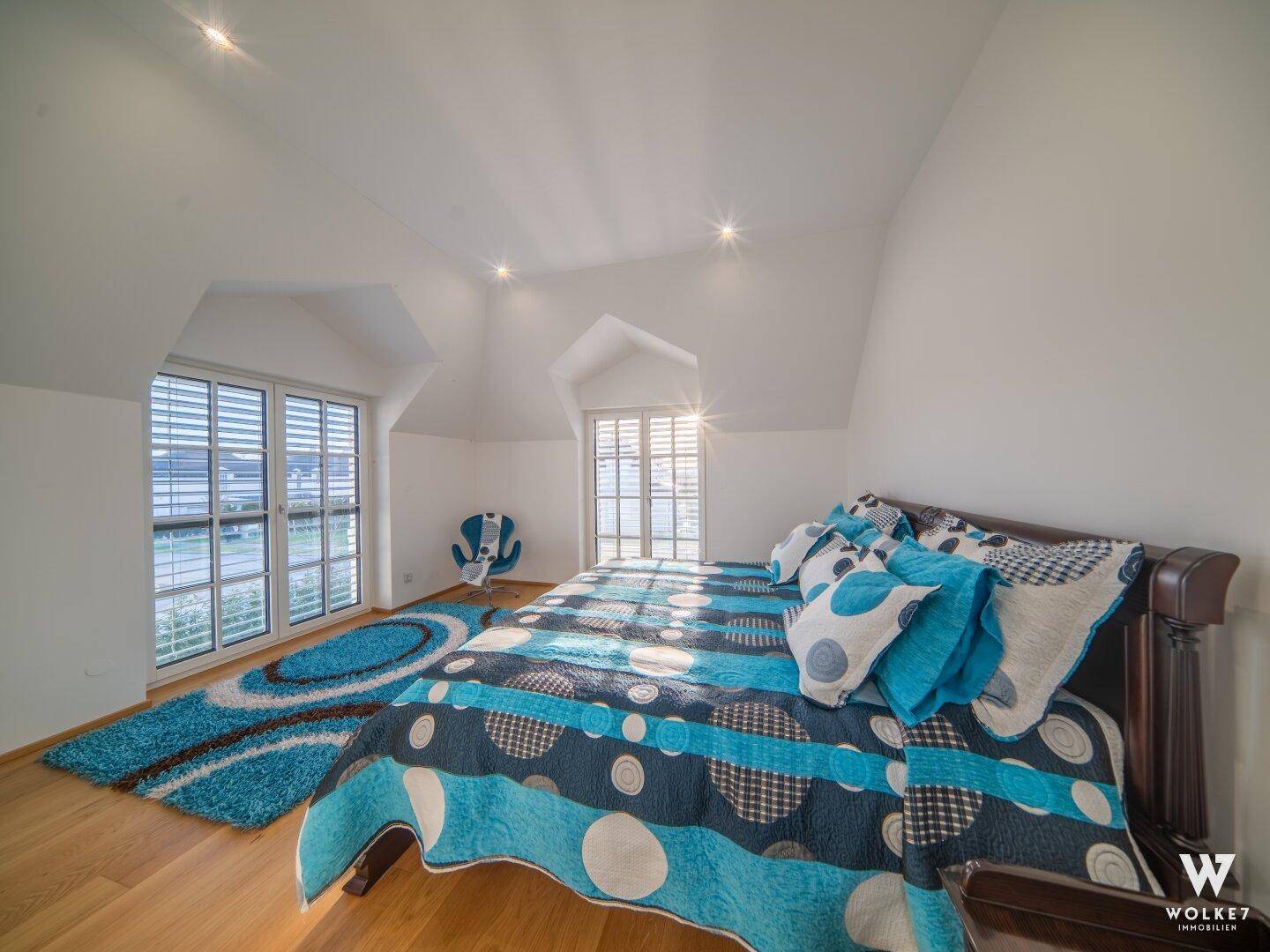 Farbenfrohes Schlafzimmer mit Holzboden, Dachschrägen und großen Fenstern.