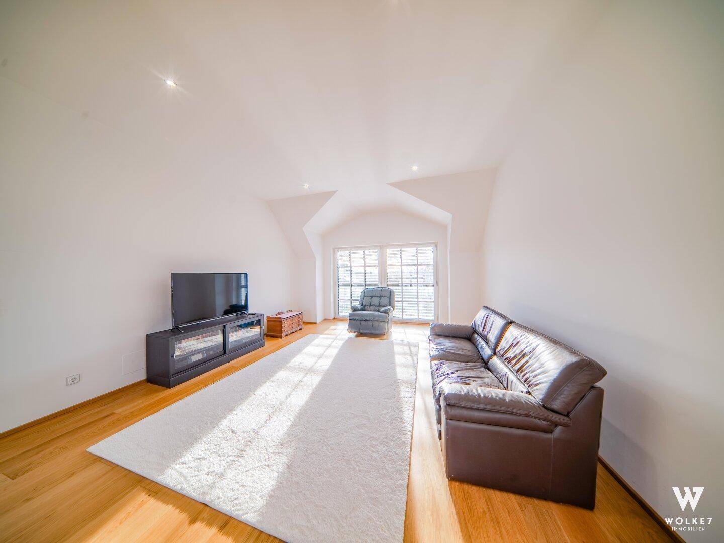 Gemütlicher Wohnbereich mit Sofa, Fernseher und viel Tageslicht im Obergeschoss.