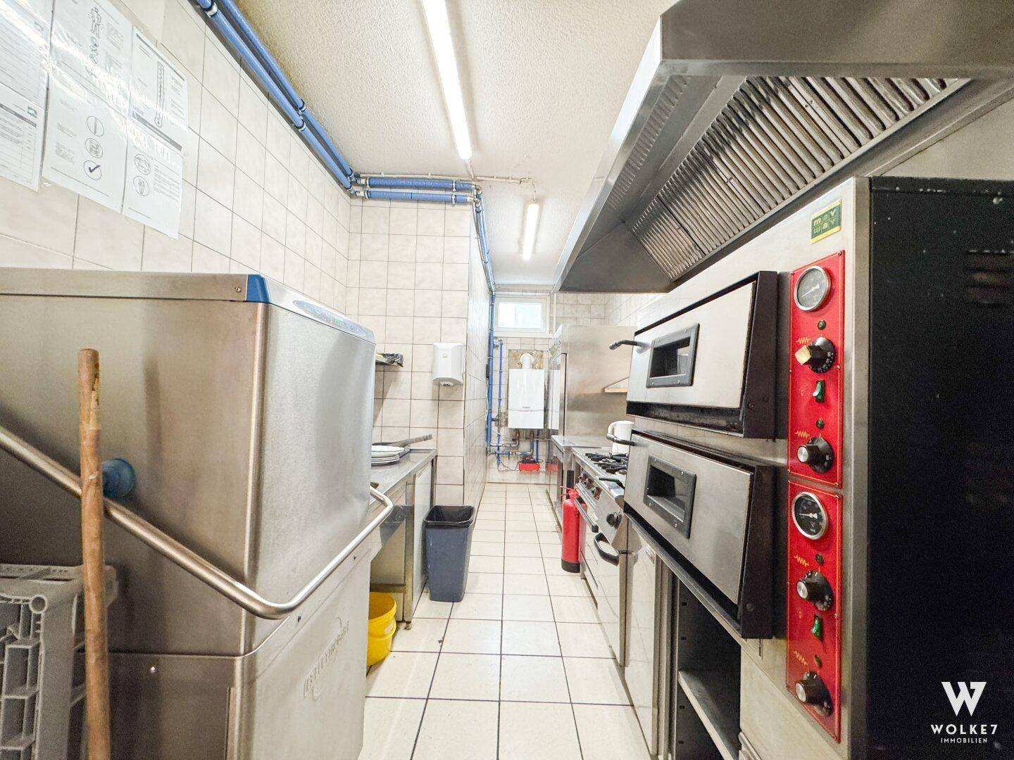 Schmale, funktionale Gewerbeküche mit Fliesenboden, Edelstahlgeräten und professionellen Öfen.