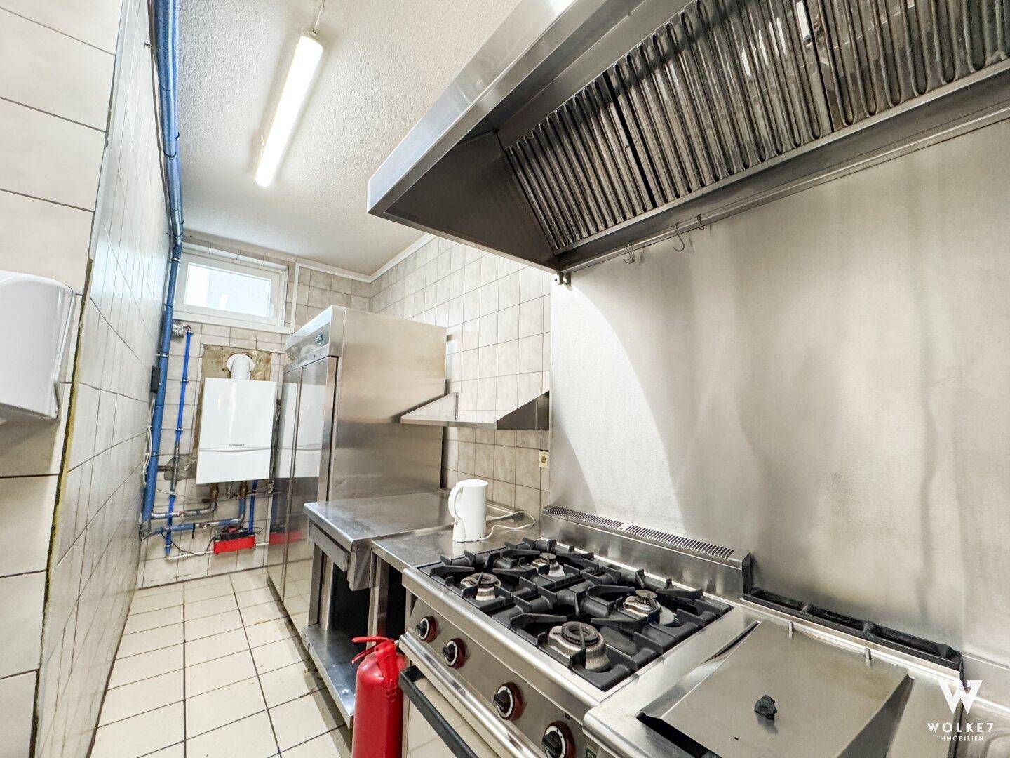 Gut ausgestattete Gewerbeküche mit Gasherd, Dunstabzugshaube und Wandfliesen für den Restaurantbetrieb.