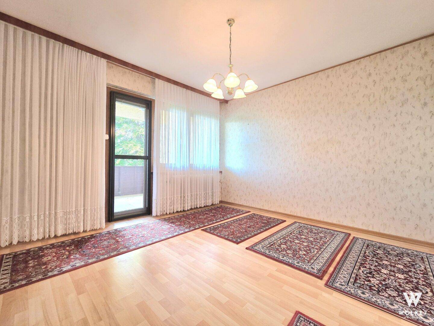 Heller Wohnraum mit Parkettboden, Zugang zum Balkon und großen Fenstern.