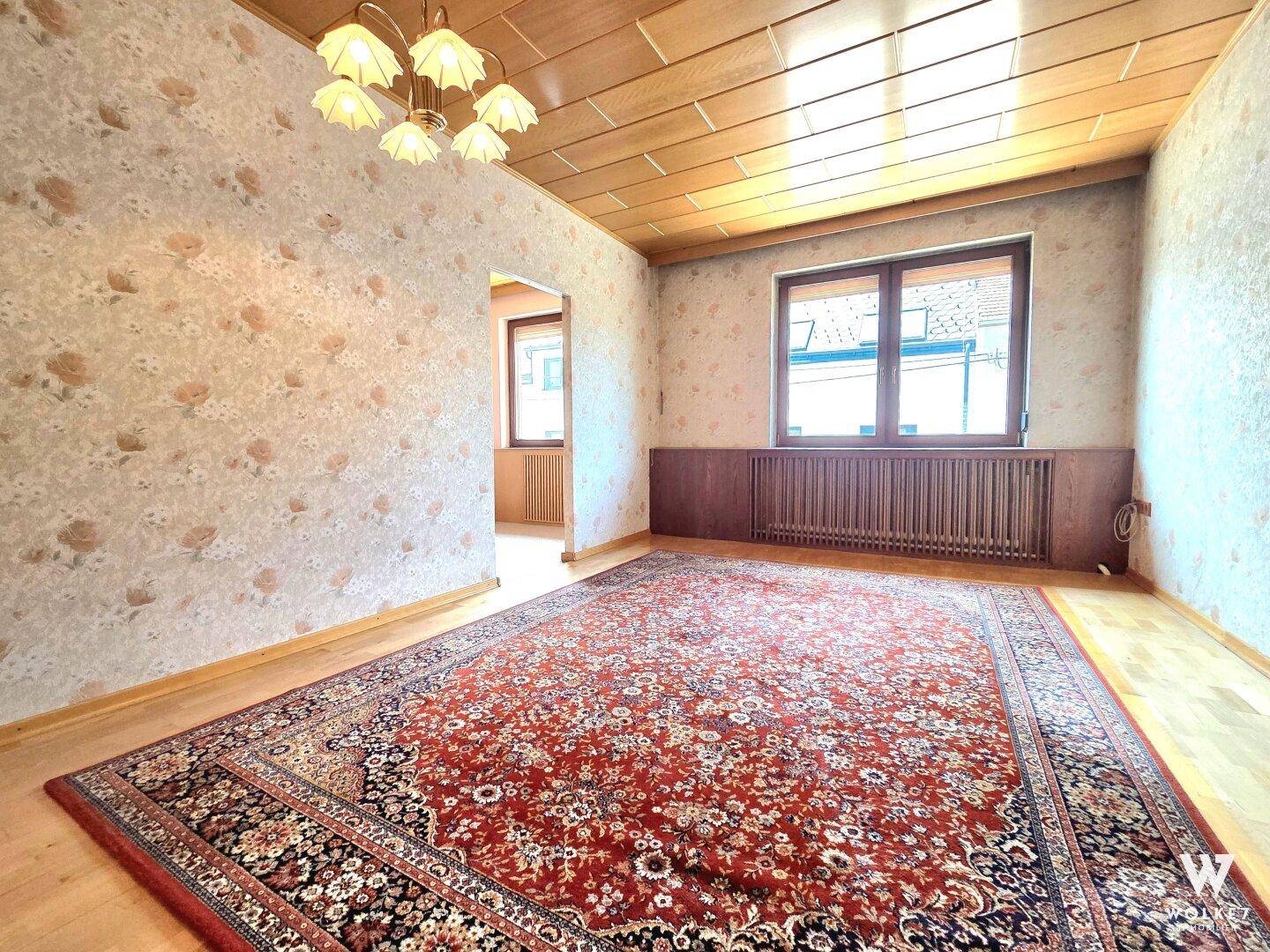 Wohnzimmer mit Holzboden, gemusterter Tapete und großem Orientteppich.