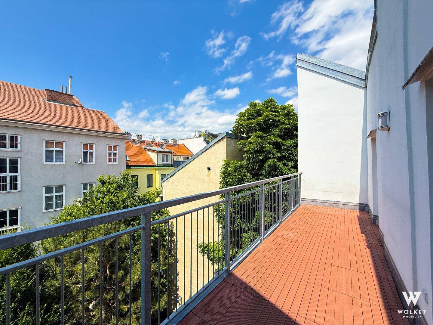 Geräumiger Balkon mit Holzboden und Blick auf die umliegenden Gebäude unter blauem Himmel.