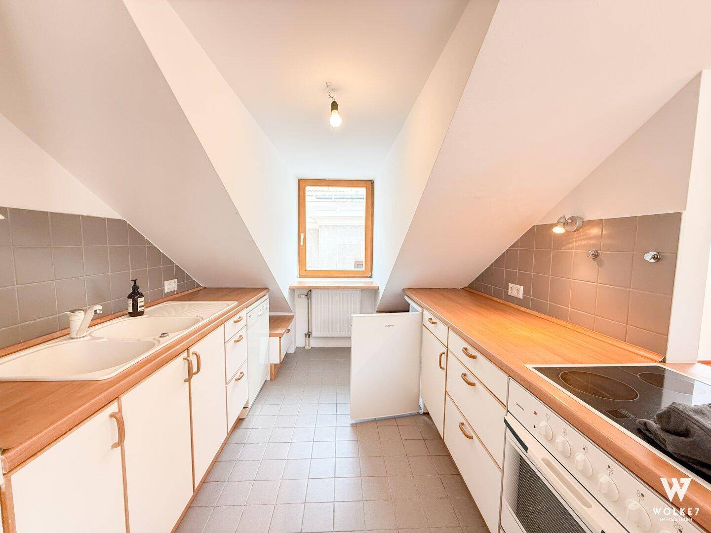 Funktionale Küche im Dachgeschoss mit Holz-Arbeitsplatten, weißen Schränken und Dachschräge.