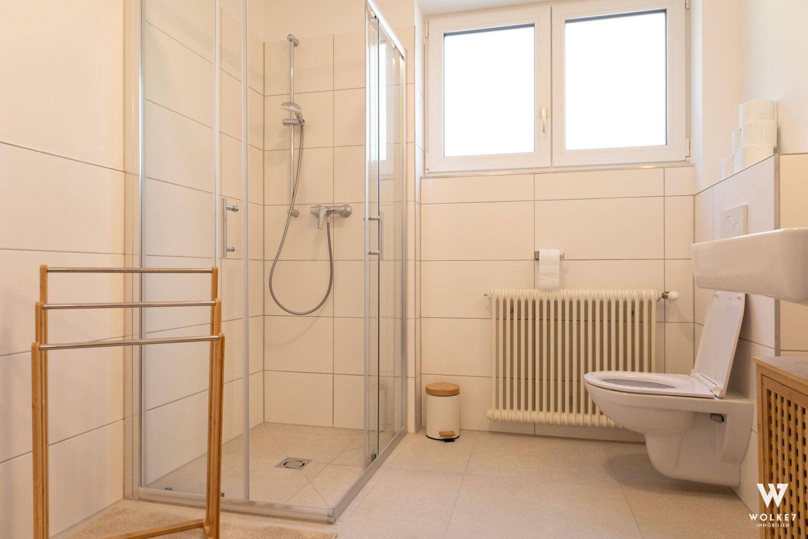 Modernes Badezimmer mit ebenerdiger Dusche, WC und Fenster für natürliches Licht.