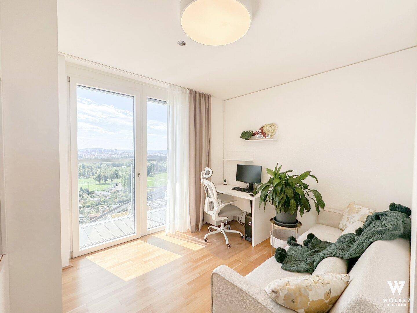 Arbeitszimmer mit Schreibtisch, Sofa und großen Fenstern, die einen weiten Ausblick bieten.