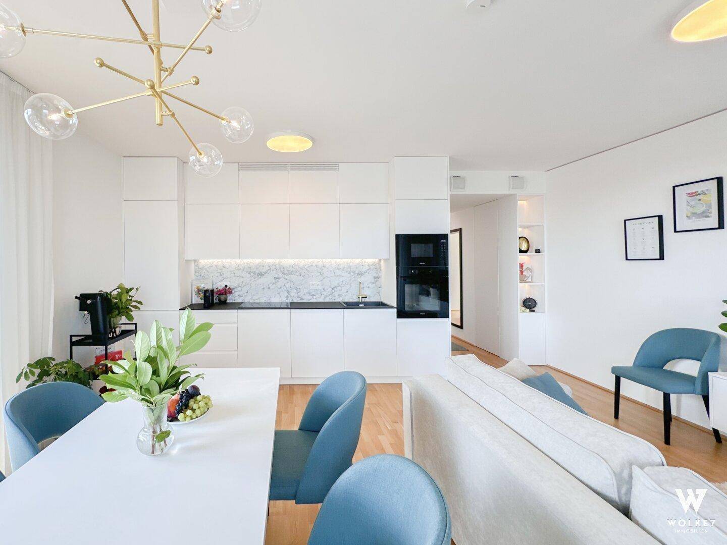 Moderne, offene Küche mit weißen Schränken, Marmorrückwand und integrierten Geräten.