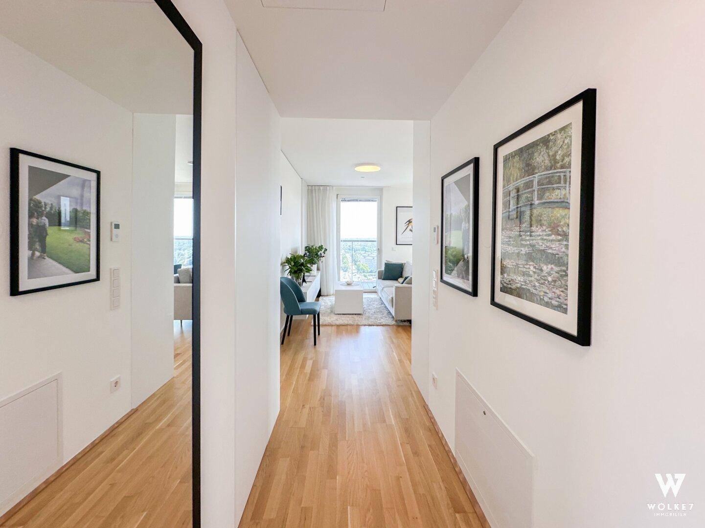 Langer, heller Flur mit Holzfußboden und Kunstwerken, der zum Wohnbereich führt.