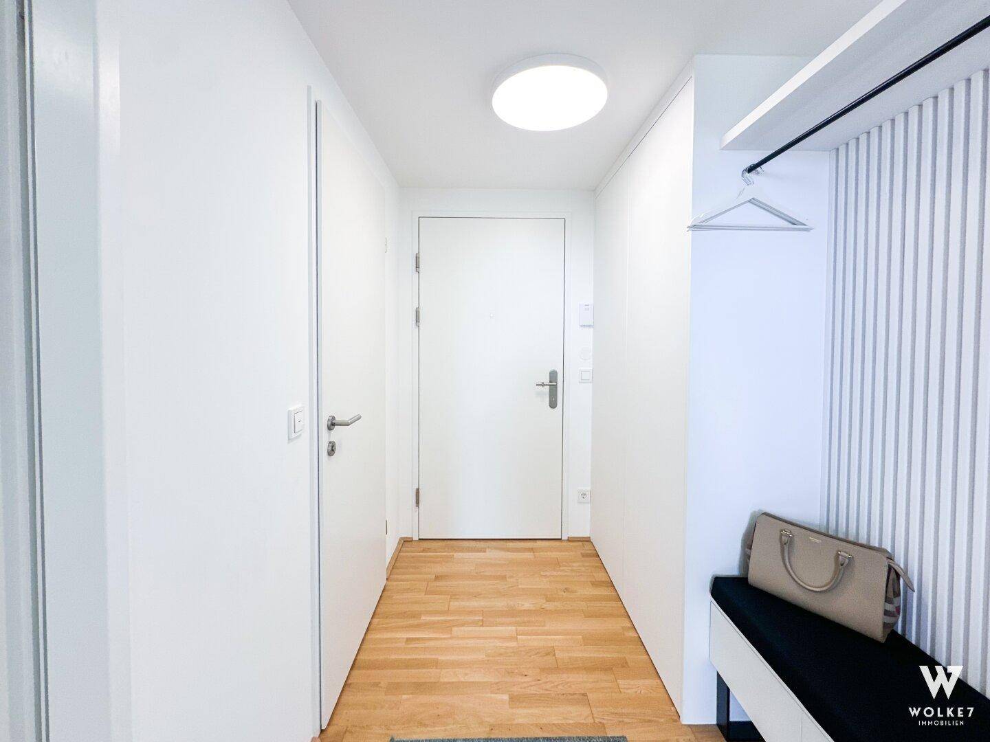 Eingangsbereich mit Garderobe, Sitzbank und hellem Holzfußboden.