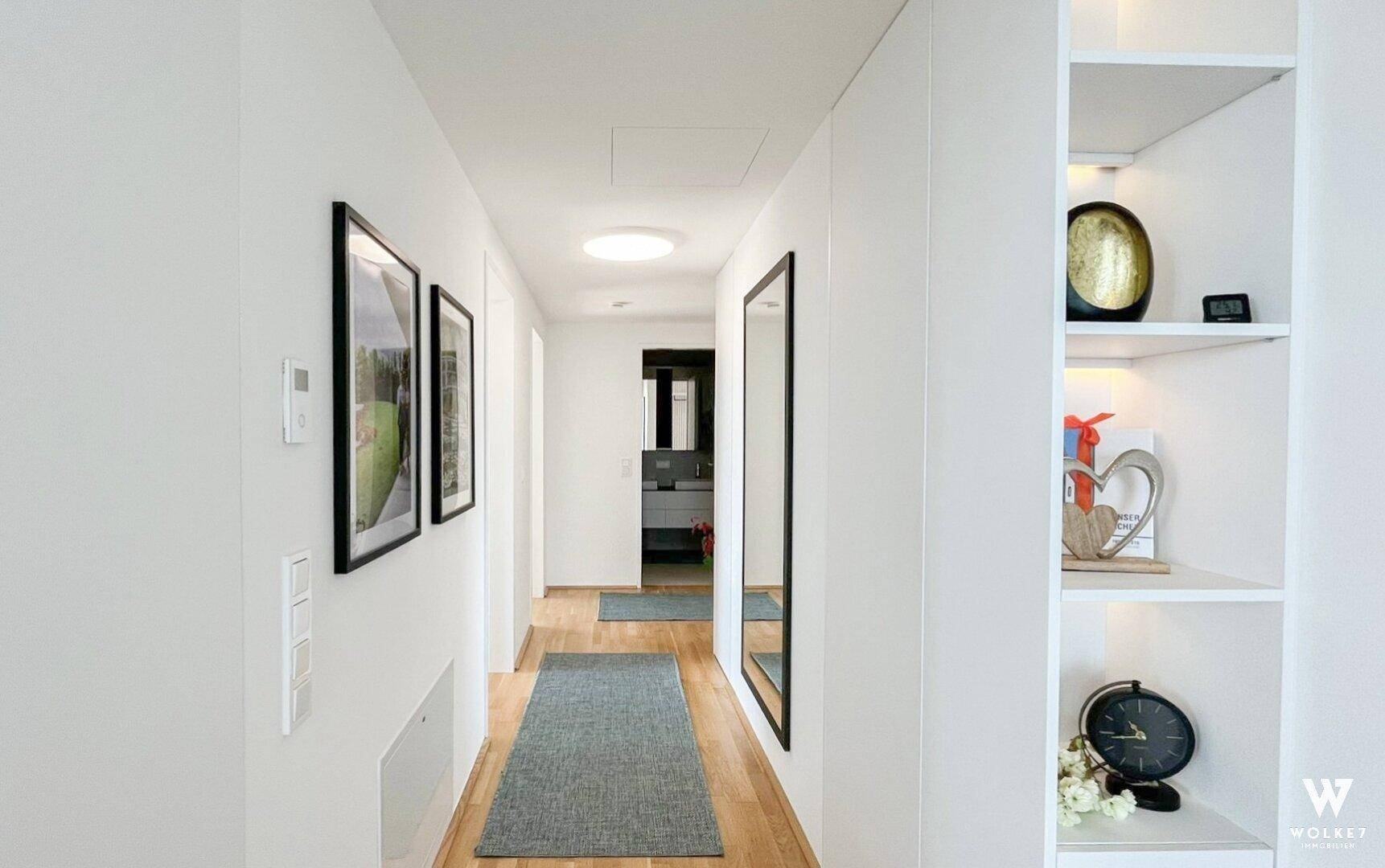 Heller Flur mit Spiegel, dekorativen Regalen und Blick in ein modernes Badezimmer.