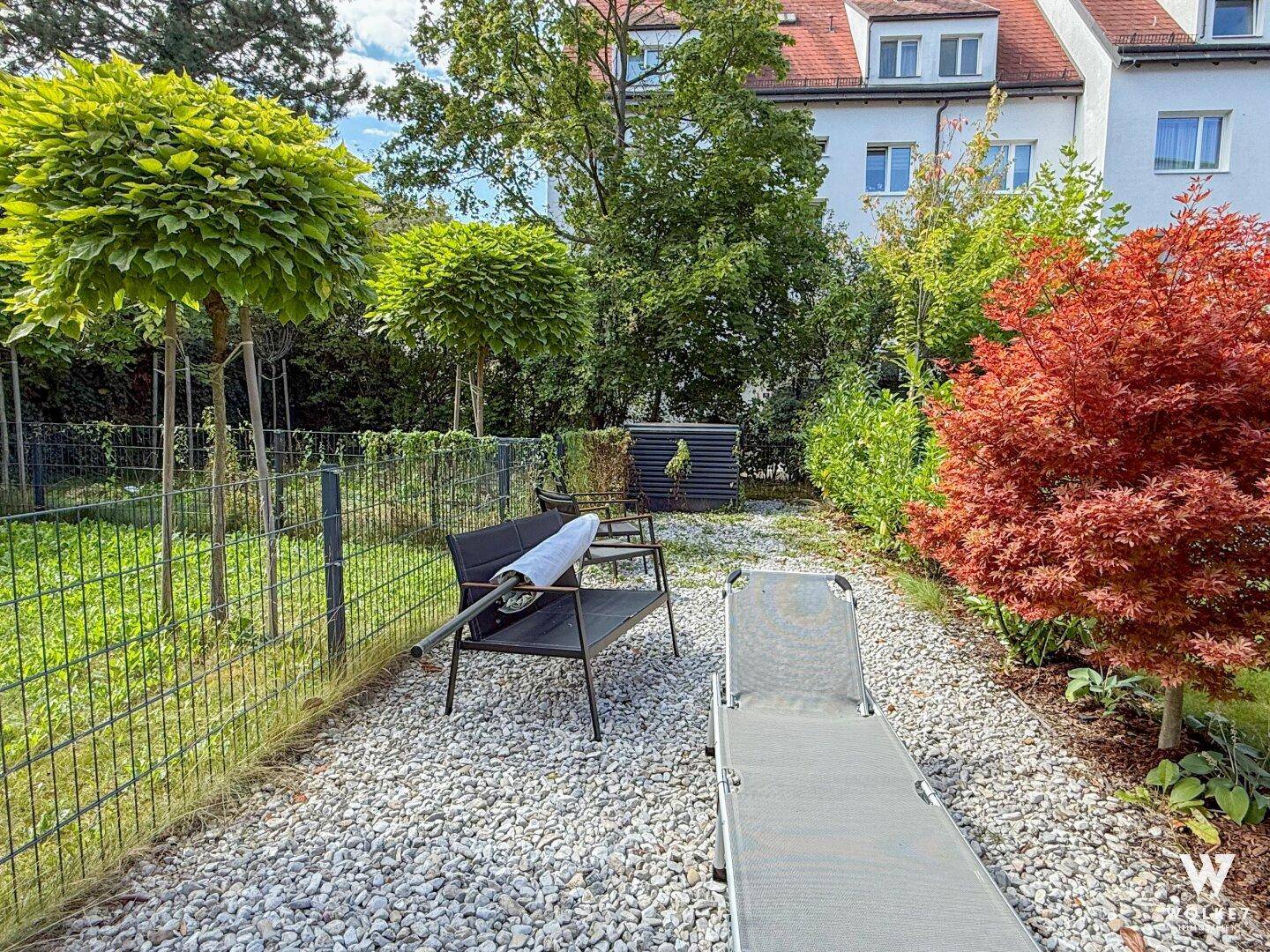 Gepflegter Gartenbereich mit Kiesweg, Liegestuhl und verschiedenen Pflanzen.