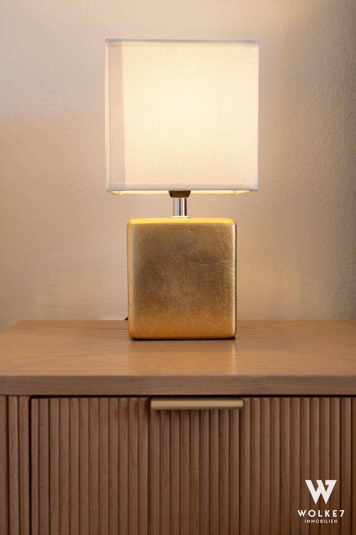 Detailaufnahme eines Nachttisches mit einer modernen goldenen Lampe, die warmes Licht spendet.