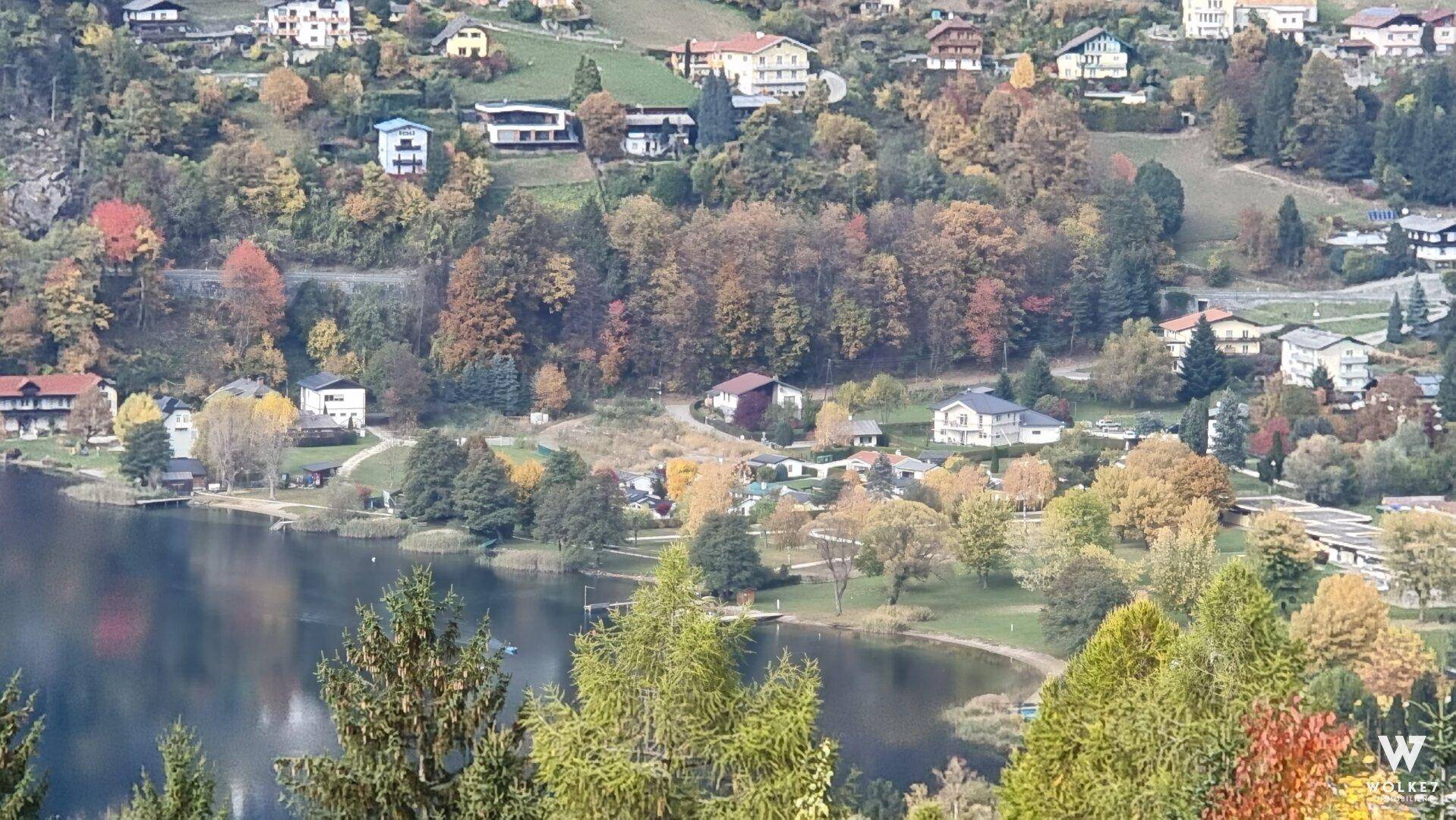 Malerischer Blick auf einen See mit umliegenden Häusern und herbstlicher Vegetation.