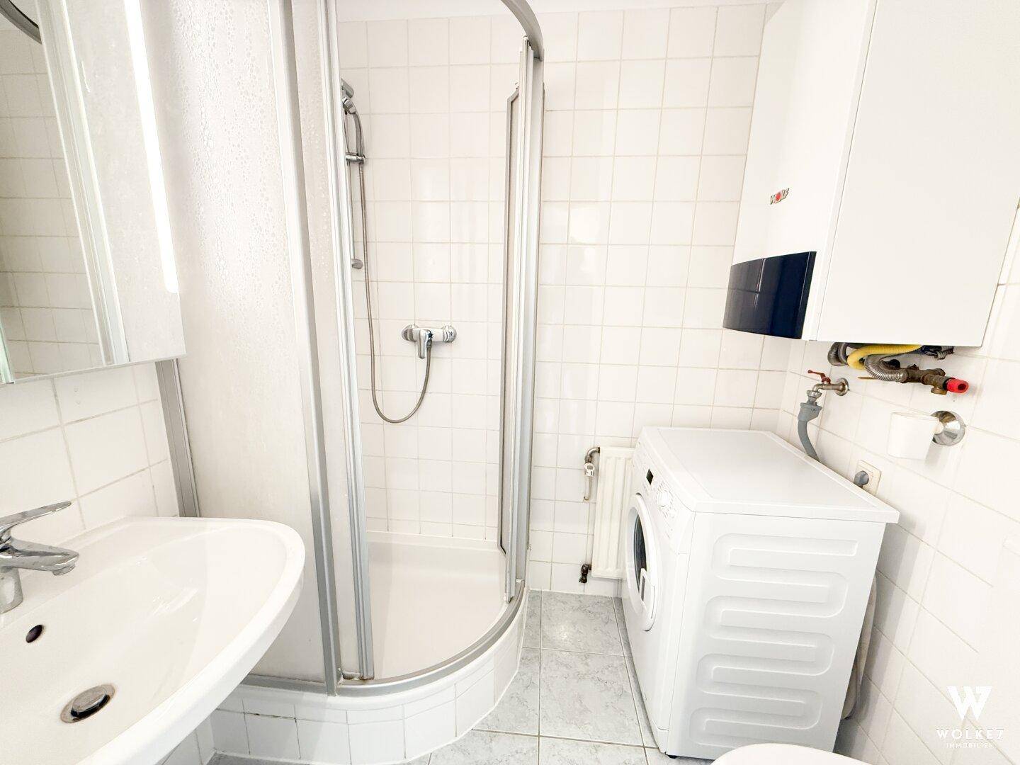 Helles Badezimmer mit Duschkabine, Waschmaschine und weißen Wandfliesen, funktional ausgestattet.