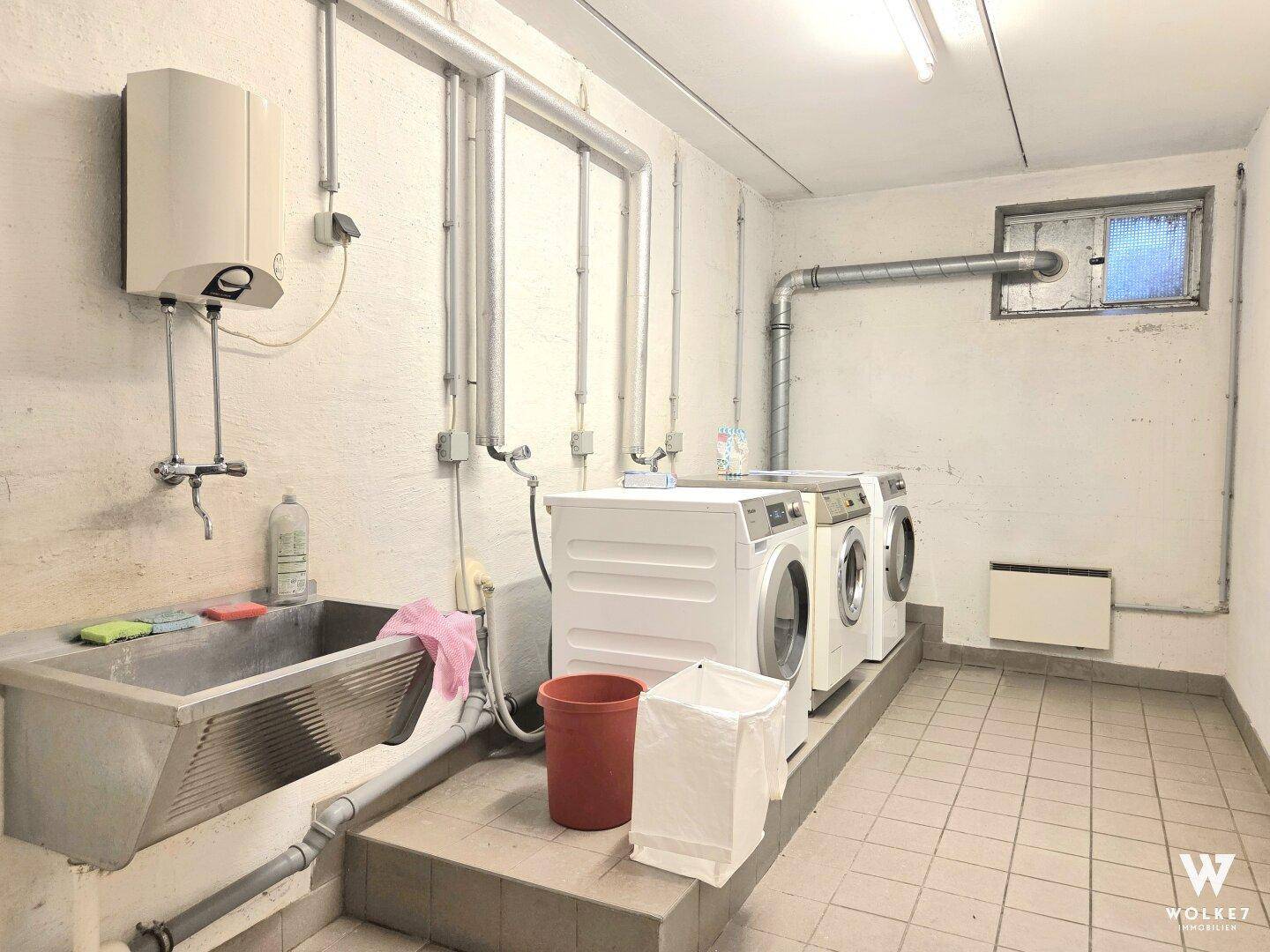 Waschküche im Keller mit Waschmaschinen, Trockner und Waschbecken.