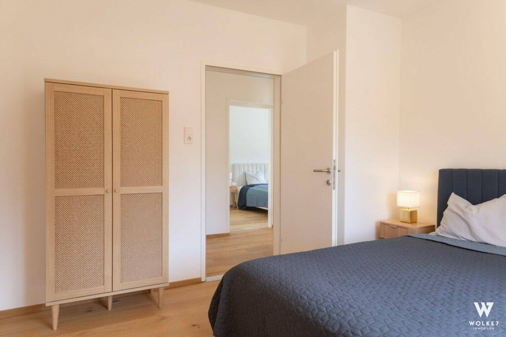 Gemütliches Schlafzimmer mit Holzboden und einem stilvollen Kleiderschrank, der zu einem weiteren Raum führt.