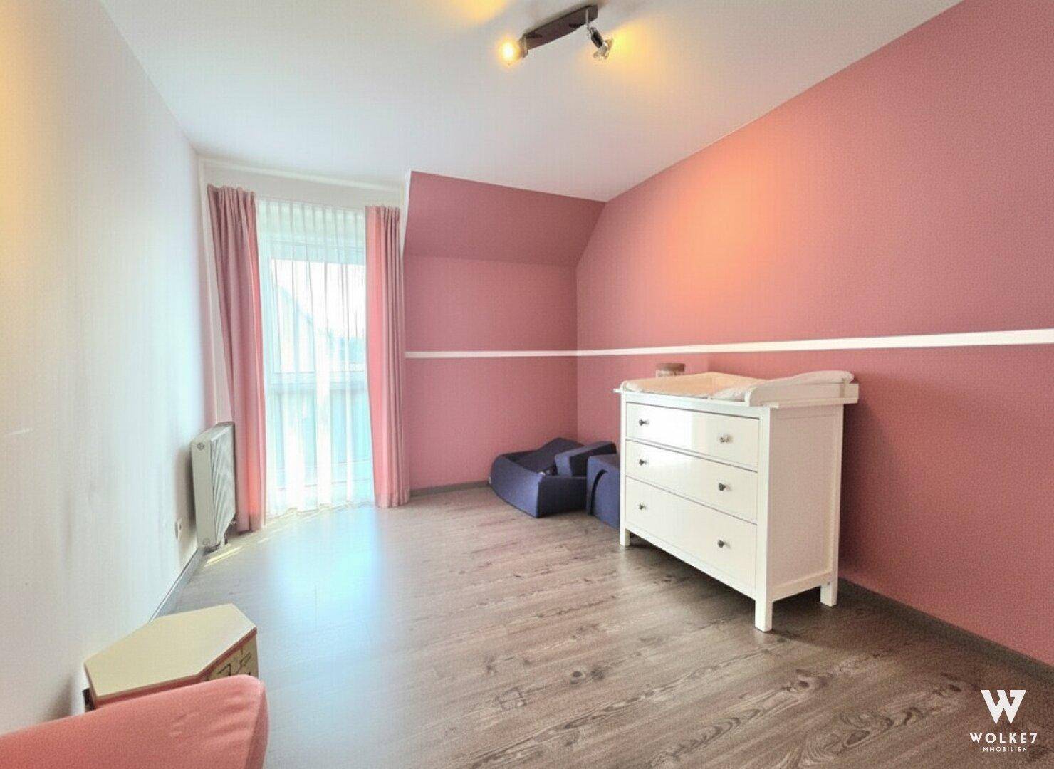 Kinderzimmer oder Schlafzimmer mit rosa Wänden, Wickelkommode und Laminatboden.