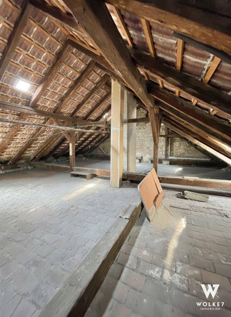 Geräumiger Dachboden mit sichtbaren Holzbalken, Dachziegeln und einem Dachfenster, bereit für den Ausbau.