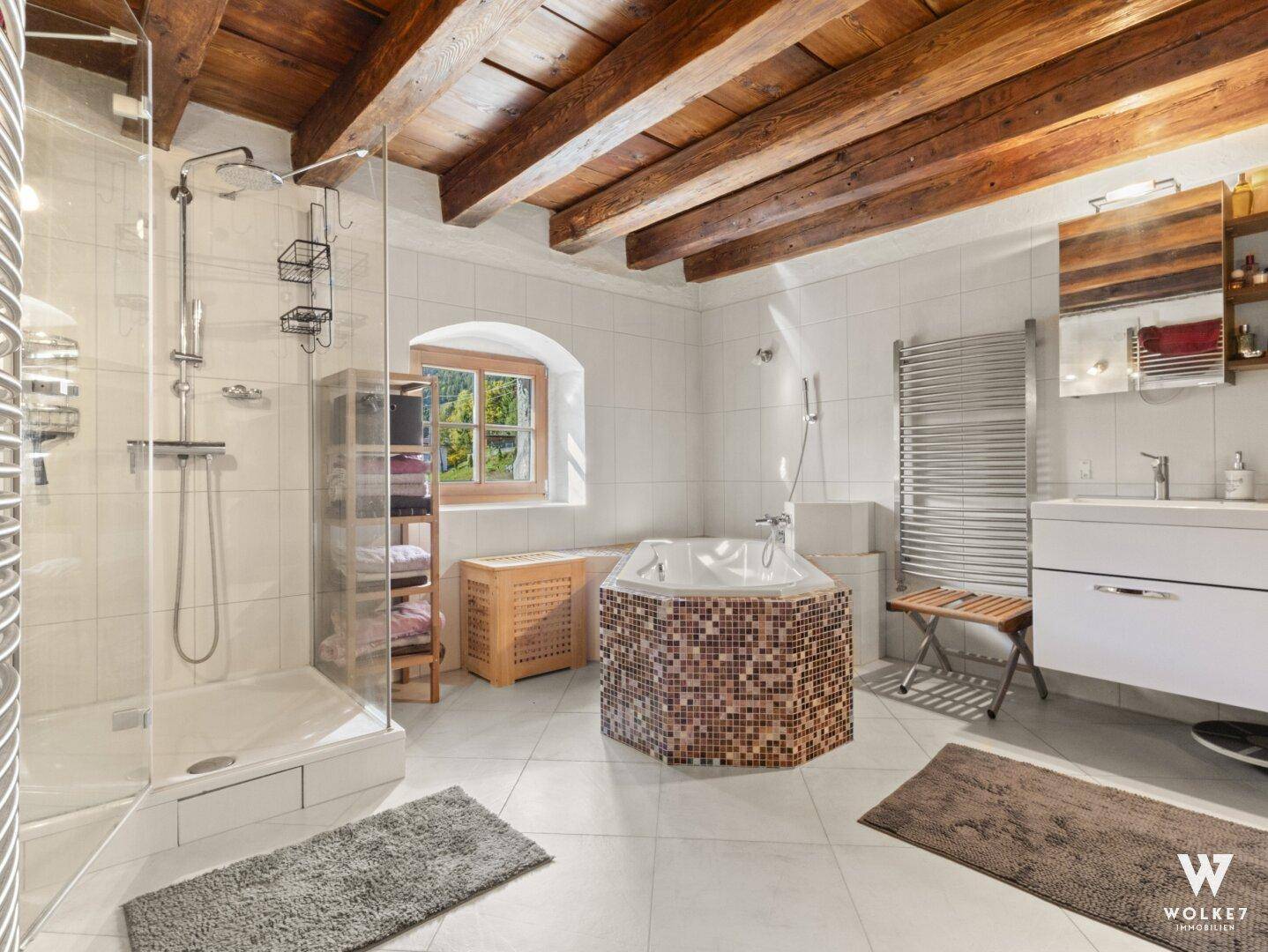 Modernes Badezimmer mit Dusche, Eckbadewanne und beheiztem Handtuchhalter unter Holzbalkendecke.