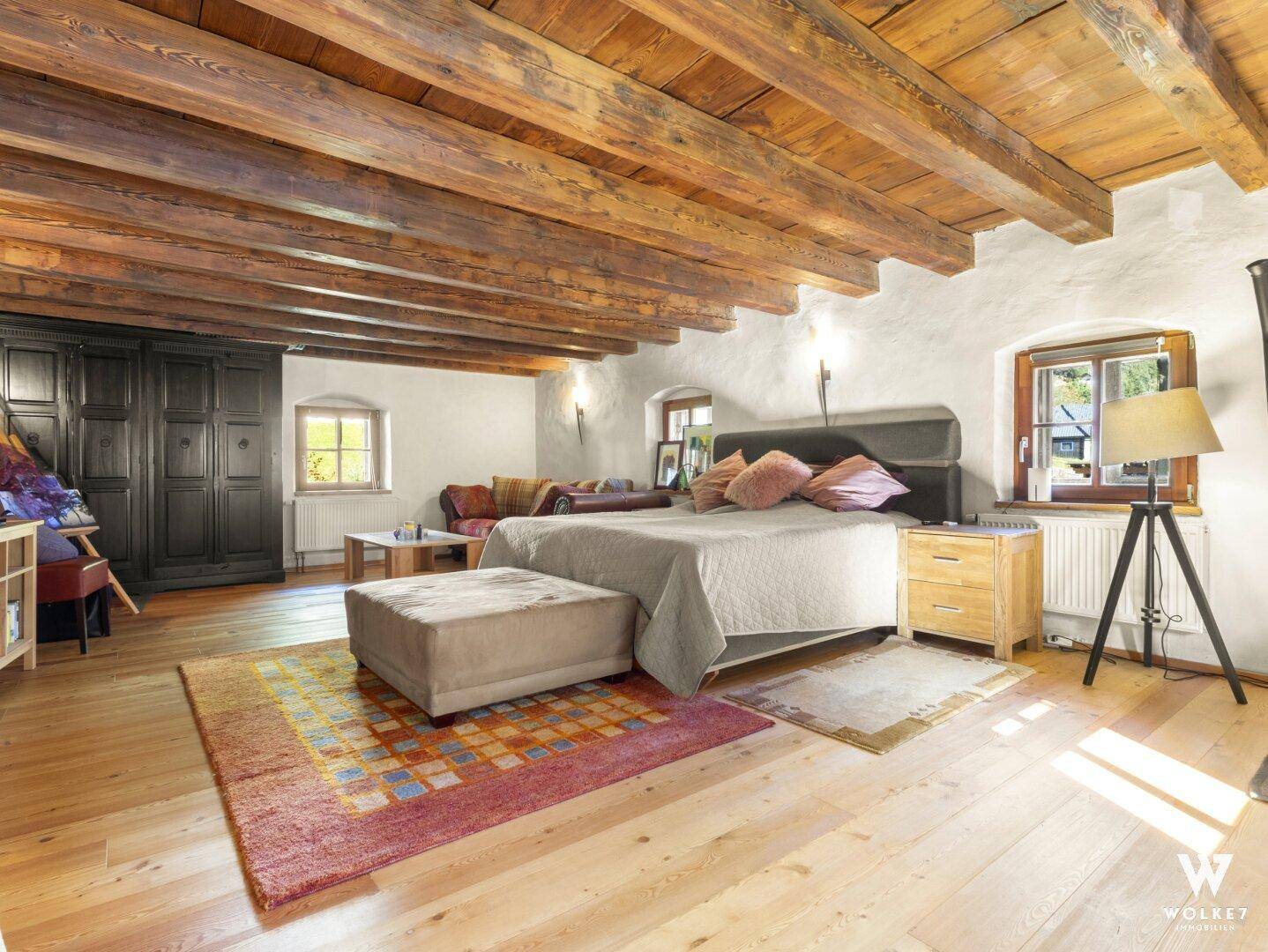 Geräumiges Schlafzimmer mit Holzbalkendecke, großem Bett und gemütlicher Sitzecke.