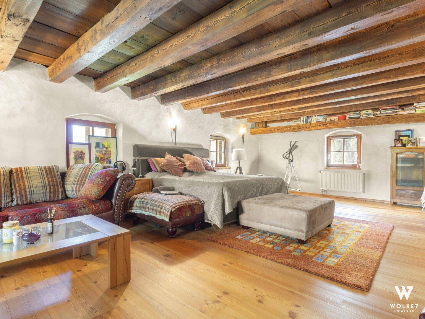 Geräumiges Schlafzimmer mit Holzbalkendecke, Parkettboden und gemütlicher Sitzecke.
