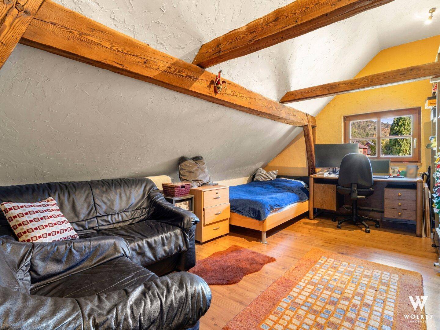 Gemütliches Schlafzimmer im Dachgeschoss mit Holzbalken, Schrägdach und Blick ins Grüne.