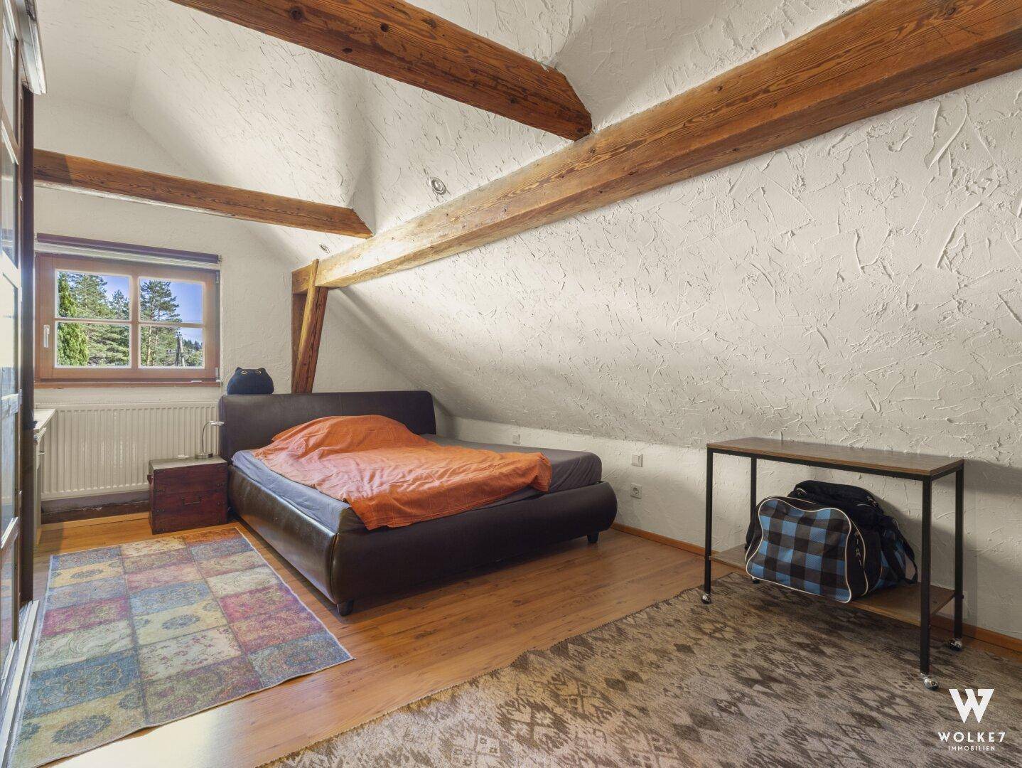 Helles Schlafzimmer im Dachgeschoss mit Holzbalken, Schrägdach und Holzboden.