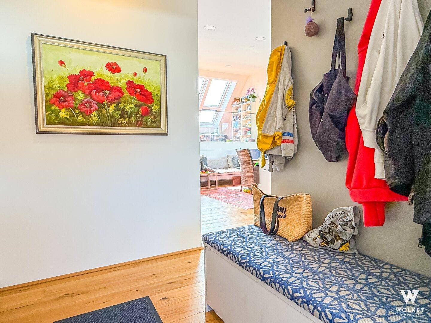 Heller Eingangsbereich mit Holzboden, einer Sitzbank und einer Garderobe, geschmückt mit einem farbenfrohen Gemälde.
