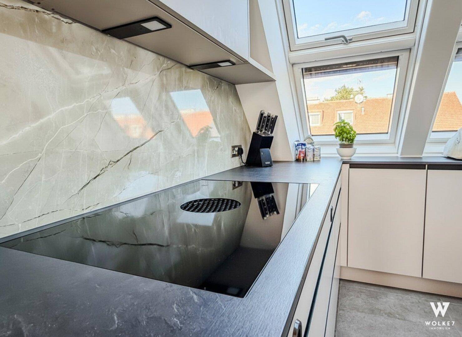 Detailansicht der modernen Küche mit Induktionskochfeld, dunkler Arbeitsplatte und eleganter Marmor-Rückwand.