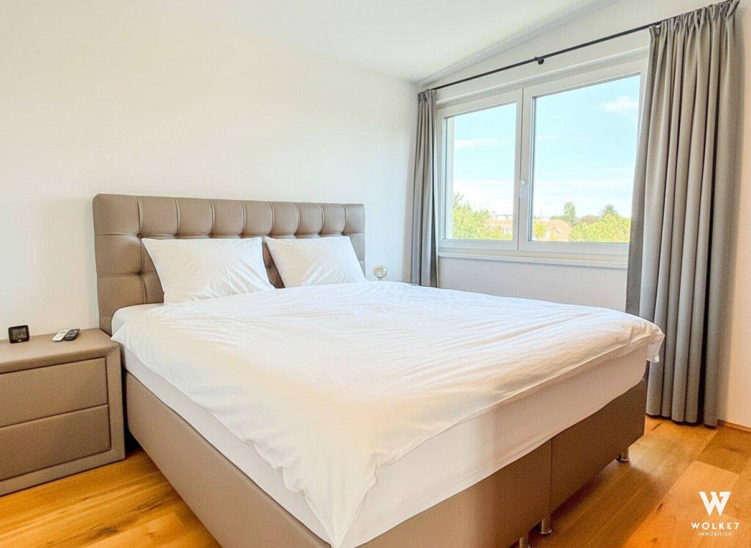 Gemütliches Schlafzimmer mit Doppelbett, Nachttischen und einem Fenster, das einen Blick ins Grüne bietet.