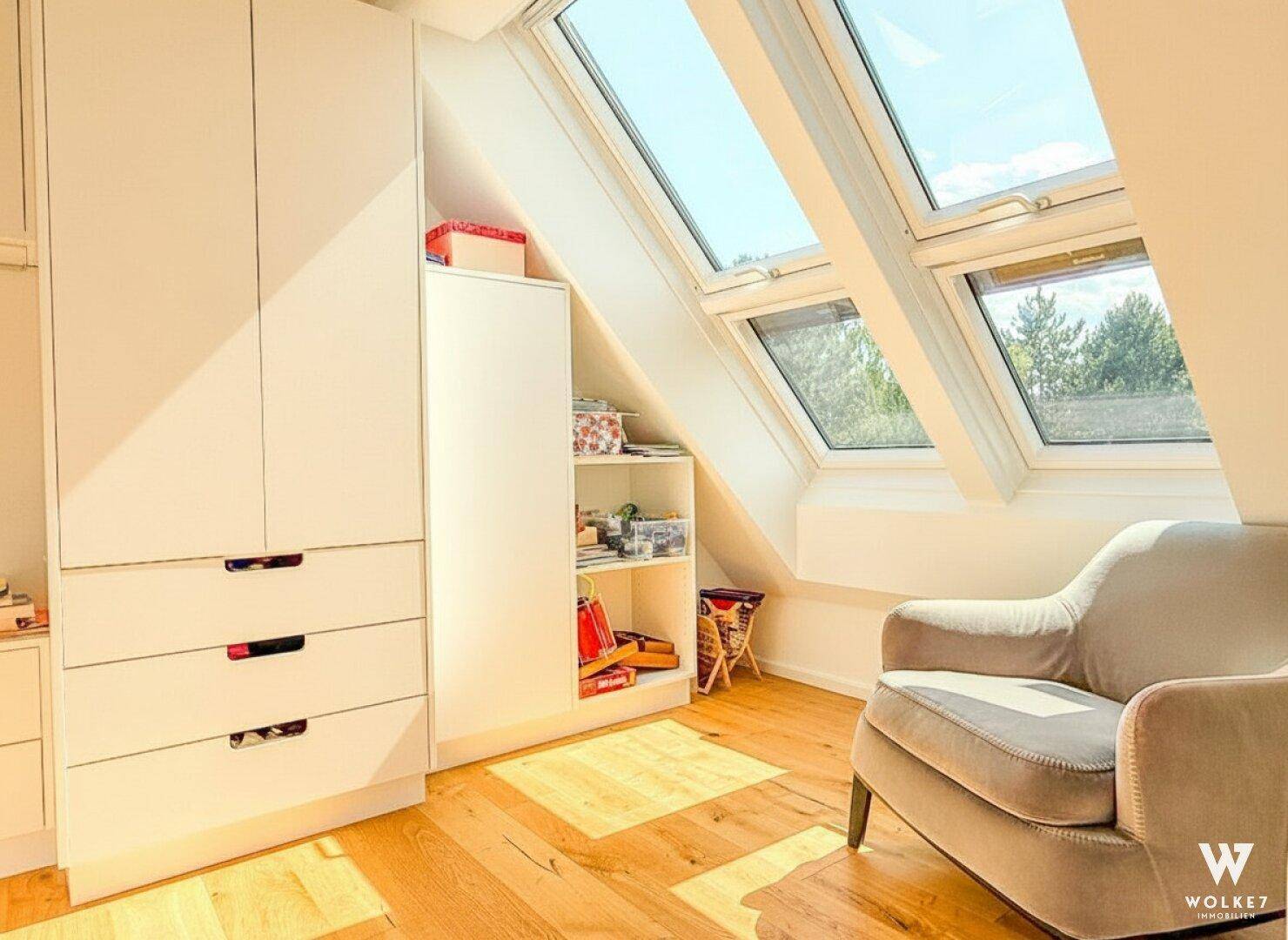 Helles Zimmer mit Dachschrägenfenstern, Einbauschränken und einem gemütlichen Sessel, ideal als Kinder- oder Gästezimmer.