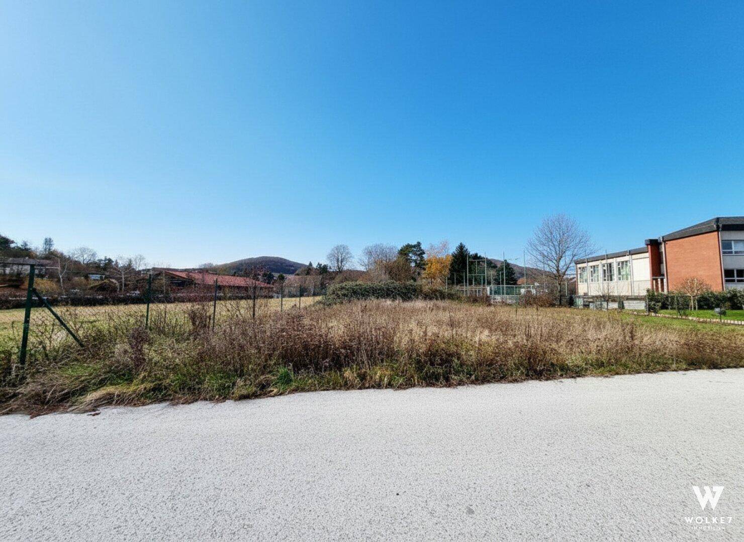 Offenes Grundstück mit weitem Blick auf die Landschaft, angrenzende Gebäude und Sportanlagen.