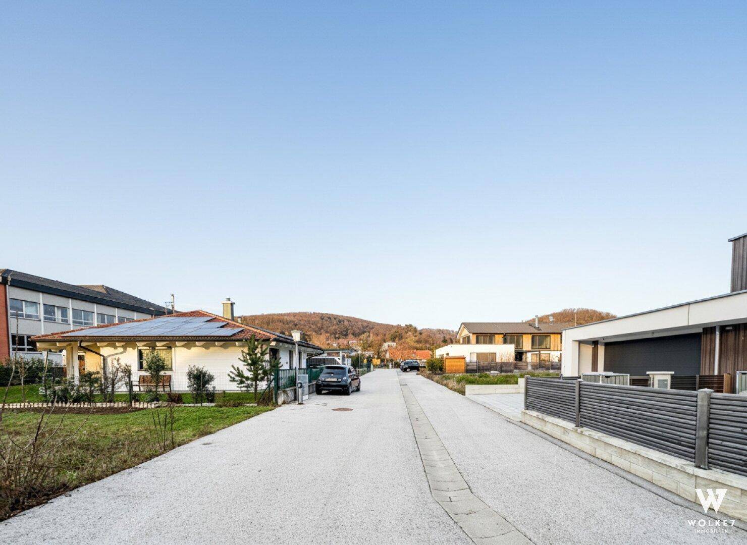 Ruhige Wohnstraße mit modernen Häusern und Blick auf die umliegende Hügellandschaft.