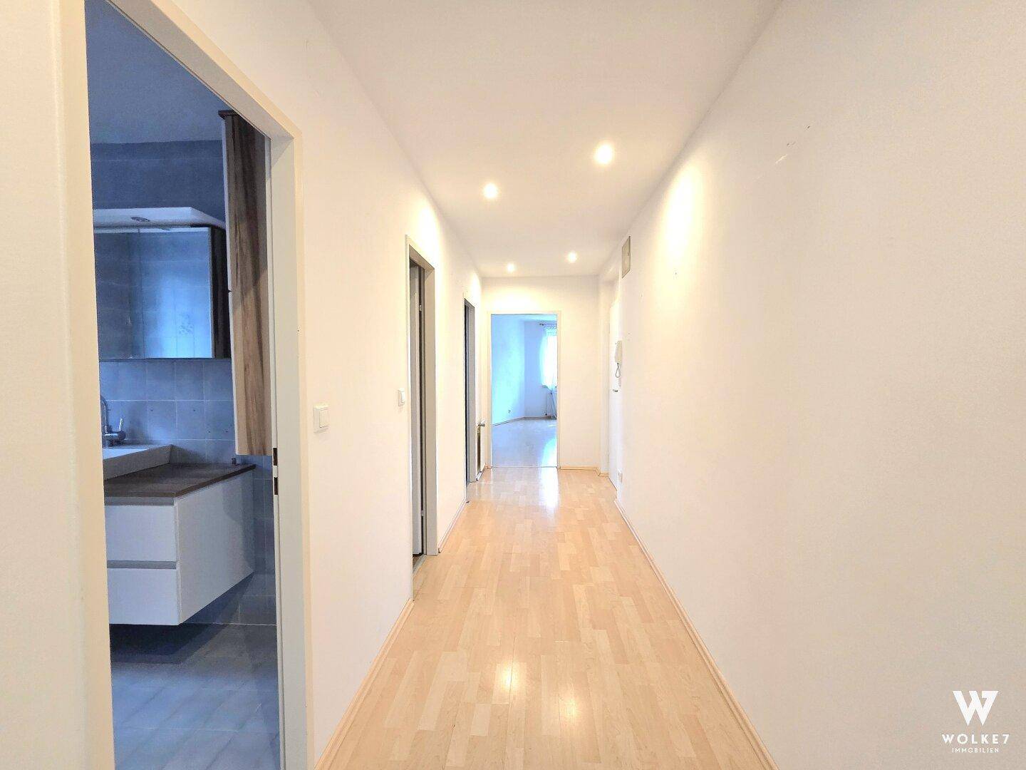 Langer, heller Flur mit Parkettboden, der zu den verschiedenen Räumen der Wohnung führt.