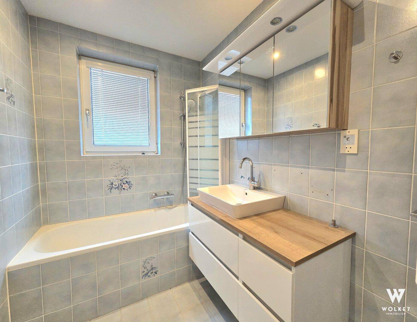 Badezimmer mit Badewanne, Dusche, modernem Waschtisch und Fenster für Tageslicht.
