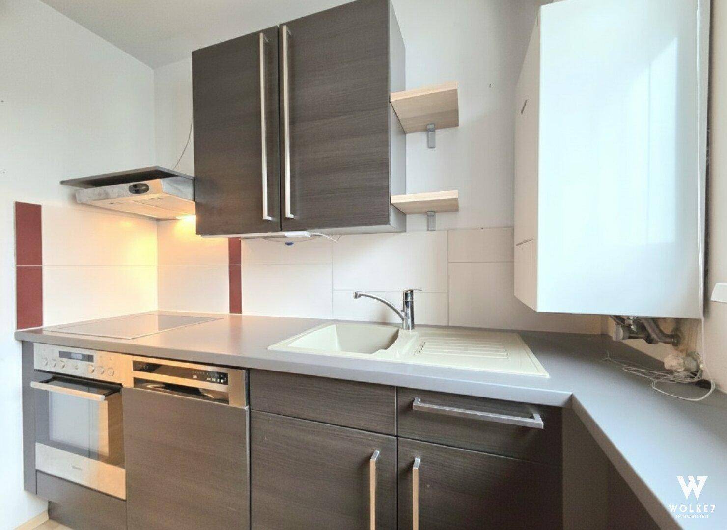Funktionale Einbauküche mit dunklen Holzschränken, grauer Arbeitsplatte und integrierten Geräten.