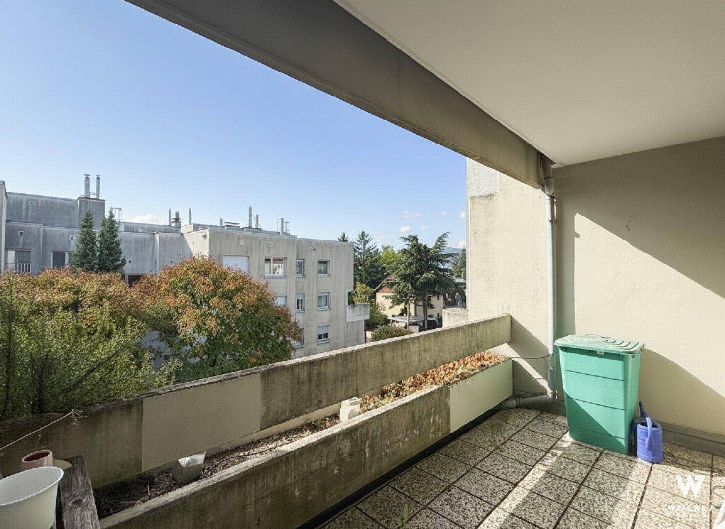 Originaler Balkon mit Fliesenboden und Ausblick auf die Nachbargebäude und grüne Umgebung.