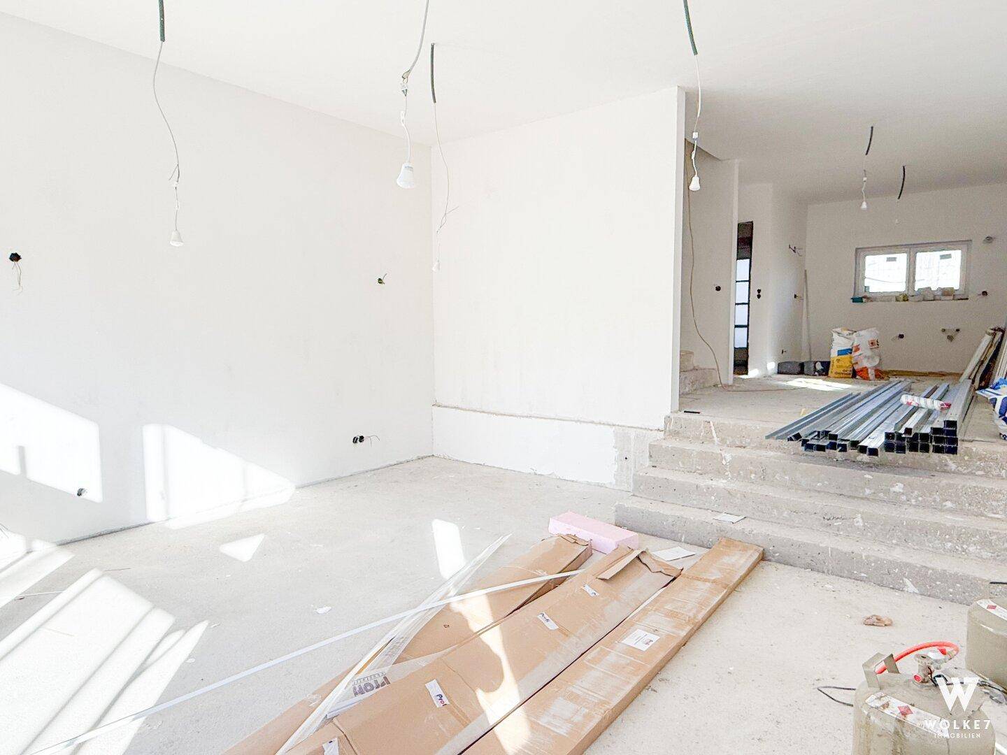 Unfertiger Wohnbereich im Rohbau mit Betonboden und Baumaterialien, bereit für den Ausbau.