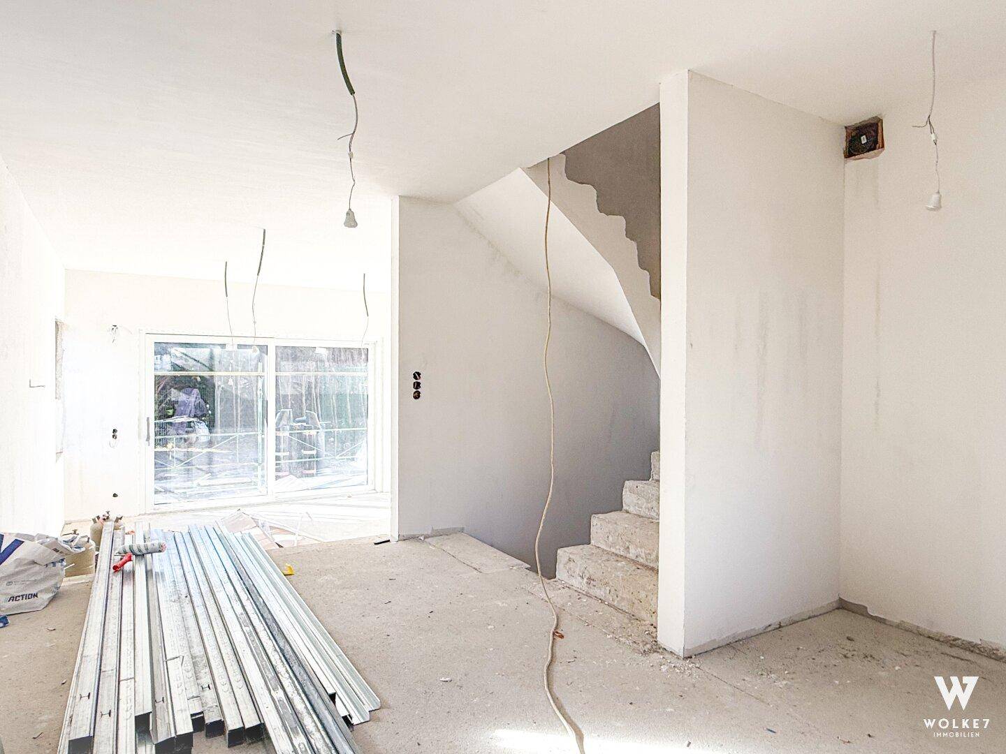Eingangsbereich im Rohbau mit offener Treppe und vorbereiteten Elektroinstallationen.