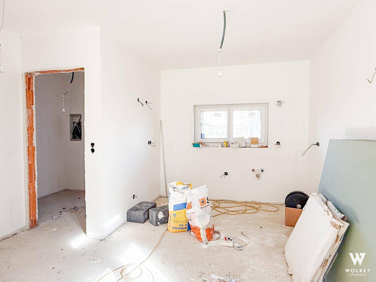 Rohbau einer zukünftigen Küche mit Fenster und vorbereiteten Anschlüssen für Geräte.
