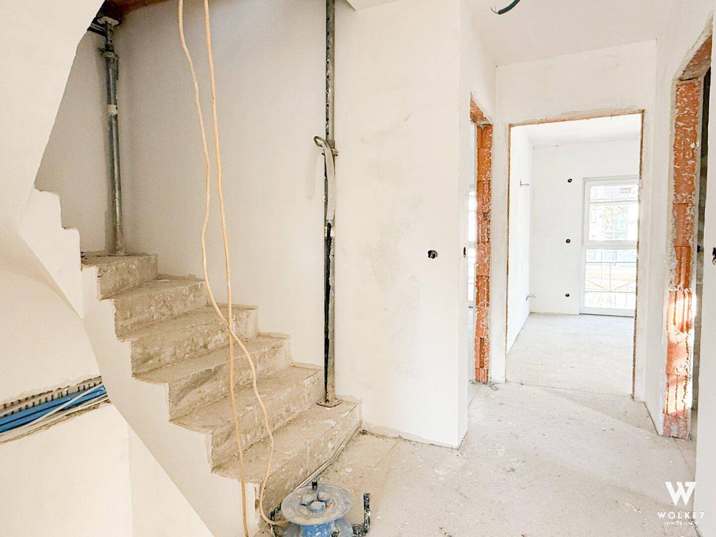 Treppenaufgang im Rohbau mit Betonstufen und sichtbaren Installationsleitungen.