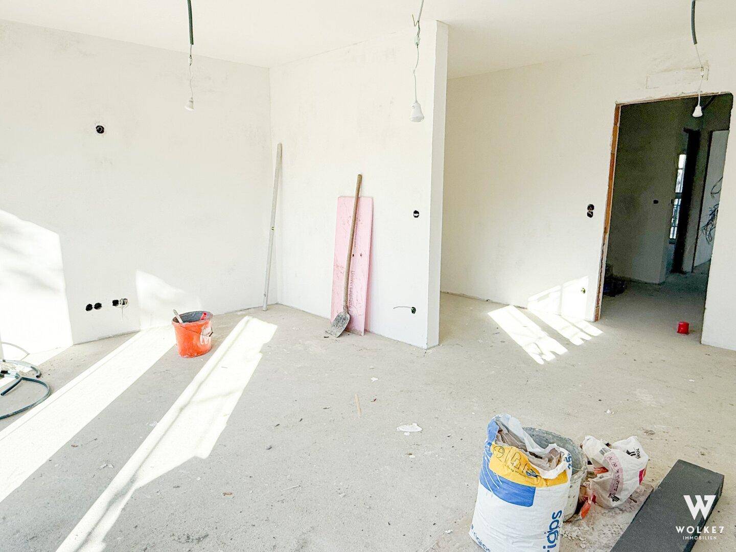 Unfertiger Innenraum mit weißen Wänden und Baumaterialien, bereit für den weiteren Ausbau.