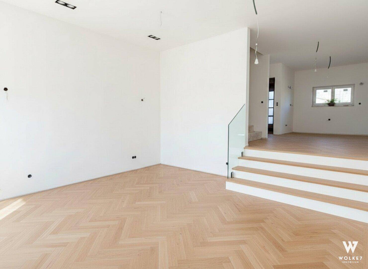 Heller Wohnbereich mit neu verlegtem Fischgrätparkett und moderner Treppe mit Glasgeländer.