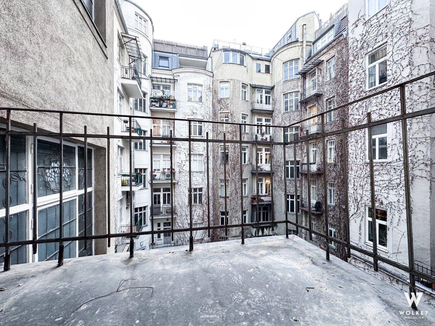 Blick von einem Balkon auf einen begrünten Innenhof mit mehreren Gebäudefassaden und Efeubewuchs.