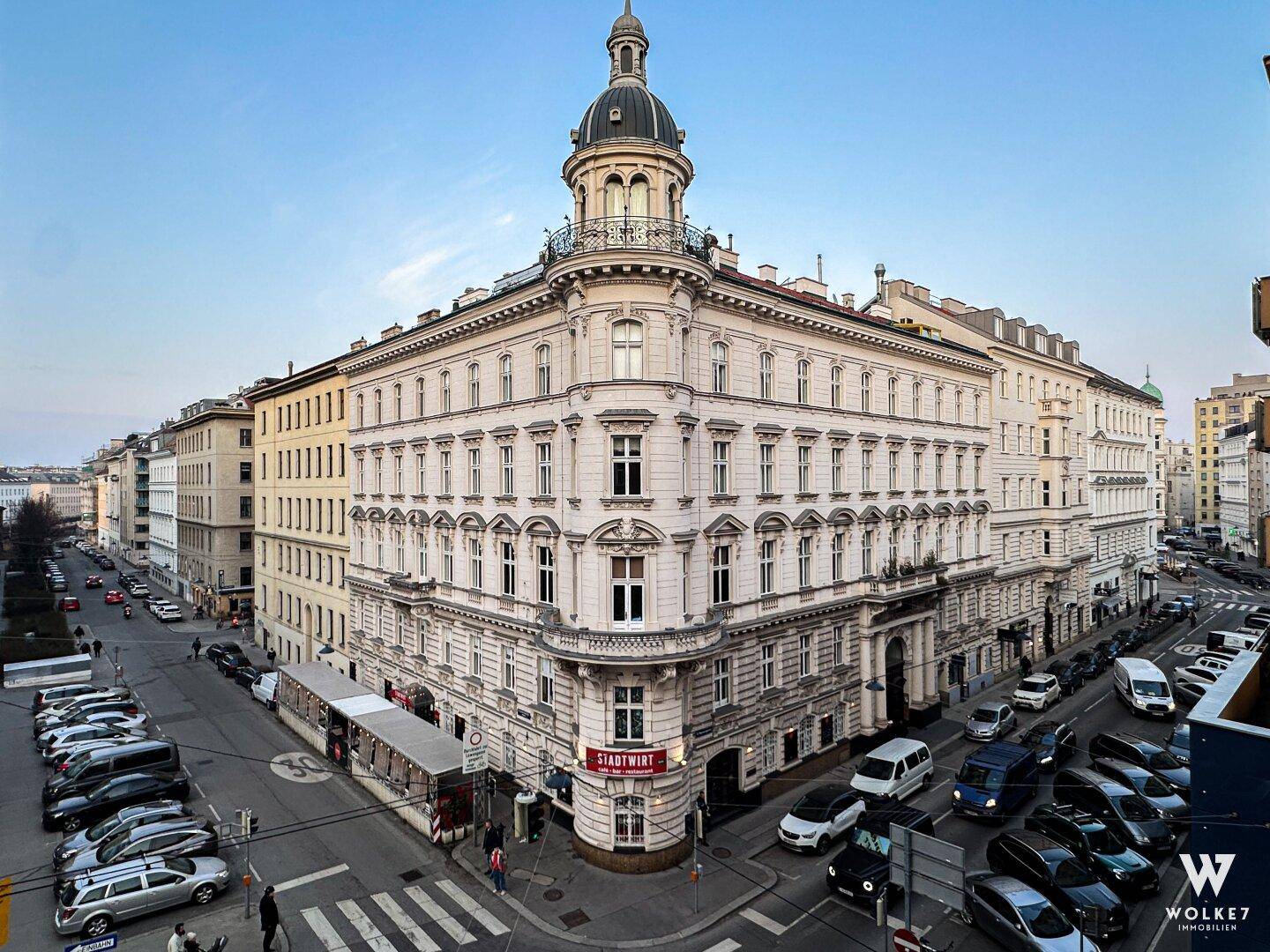 Historisches Eckgebäude mit prächtiger Architektur, Kuppel und vielen Fenstern, umgeben von städtischem Leben.