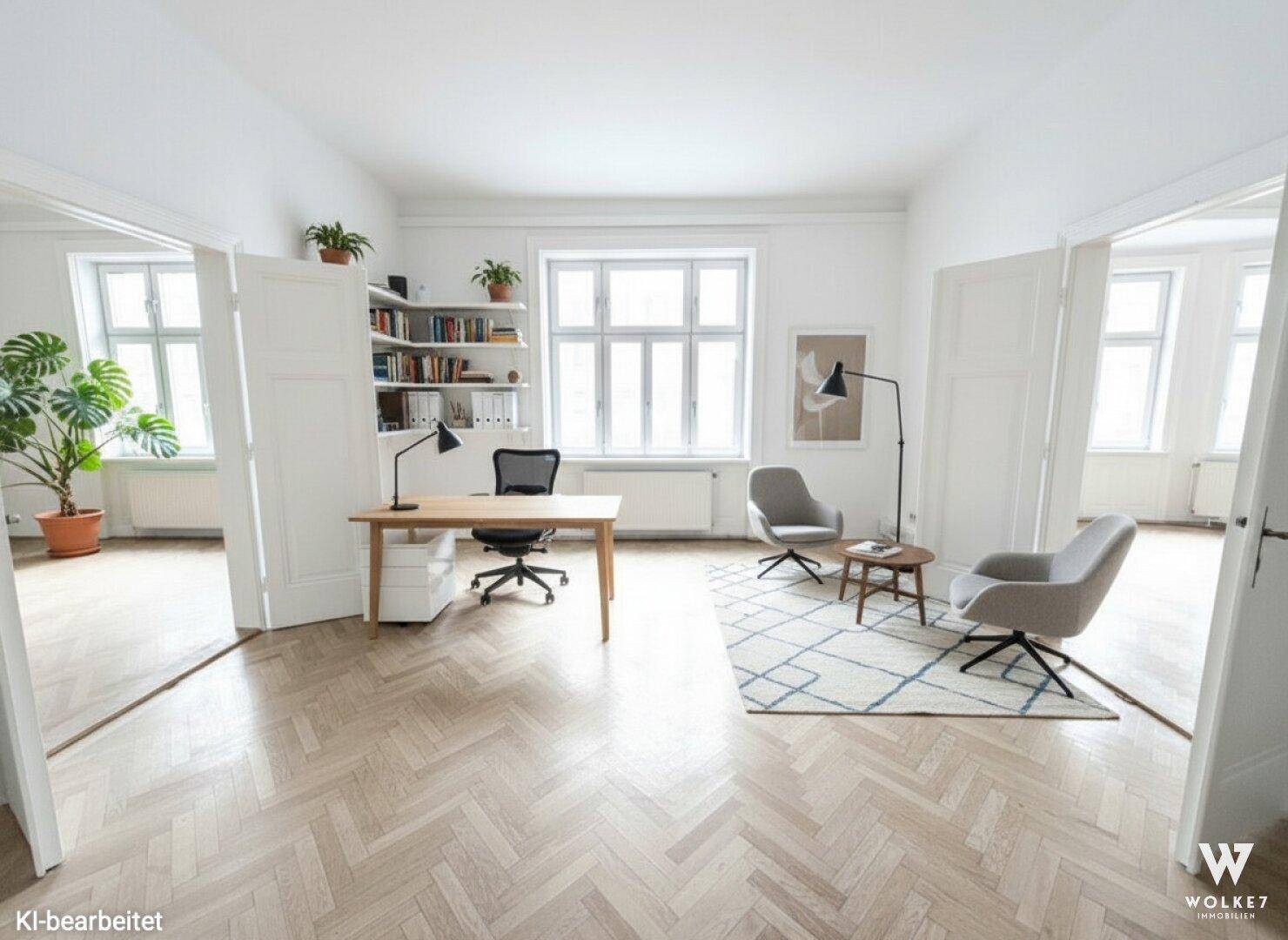 Heller Büroraum mit Fischgrätparkett, modernem Schreibtisch, Bücherregal und gemütlicher Sitzecke am Fenster.