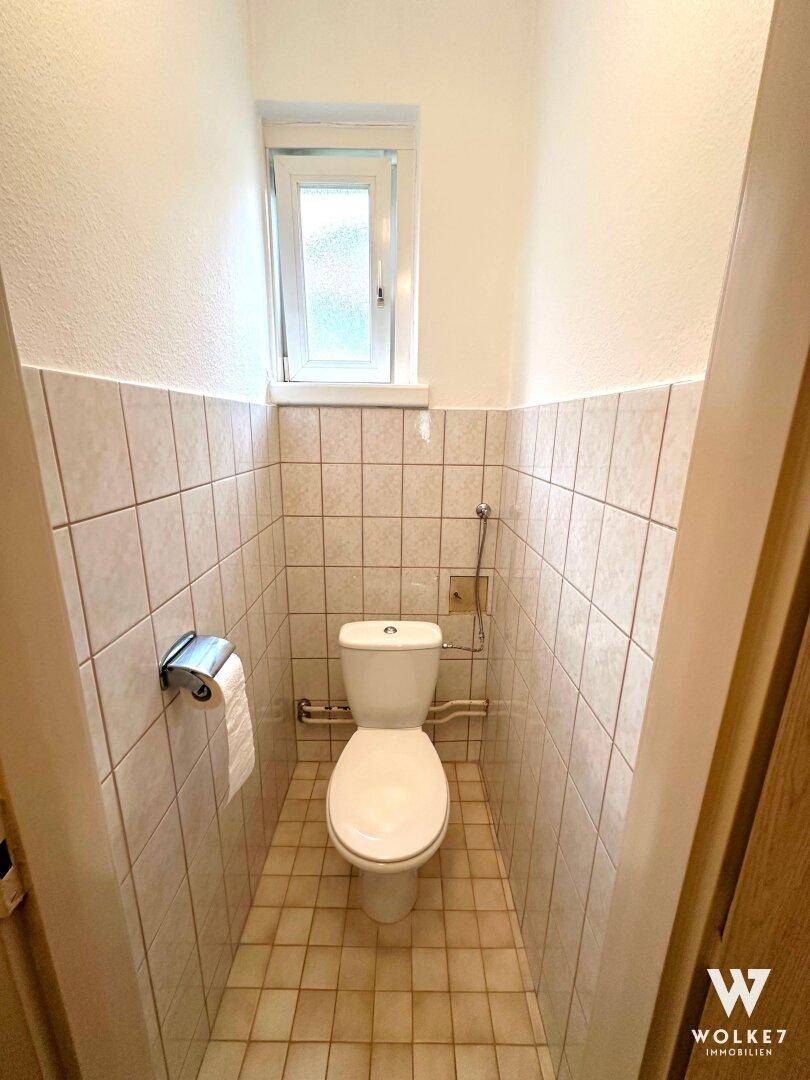 Kleines Gäste-WC mit Fenster, gefliesten Wänden und Boden in hellem Beige.