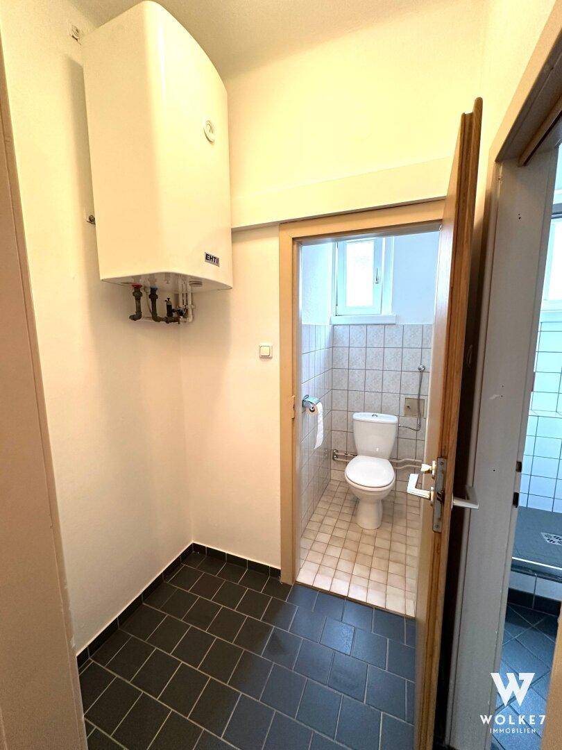 Flur mit Warmwasserboiler und Zugang zu WC und Dusche, ausgestattet mit dunklen Fliesen.