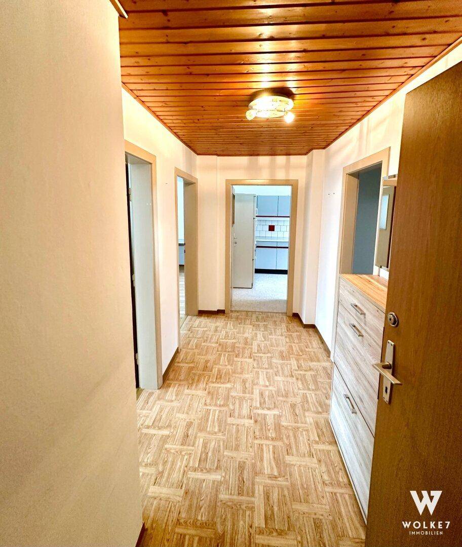 Langer Flur mit Holzdeckenverkleidung und gemustertem Bodenbelag, der zu weiteren Räumen führt.